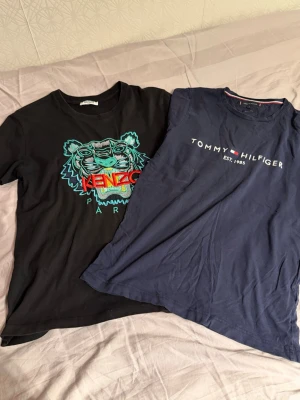 Kenzo och Tommy Hilfiger t-shirts - Två snygga t-shirts, en svart Kenzo med färgglad tiger och logga framtill, samt en mörkblå Tommy Hilfiger med tryckt logga och text. Båda har rund hals och korta ärmar, perfekta till jeans eller shorts.