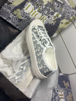 Dior Oblique låga sneakers - Snygga låga sneakers från Dior med det klassiska gråa och vita Oblique-mönstret. Skorna har vita snören, vit sula med Dior-logga och ovandel i canvas. Perfekta för dig som vill ha en exklusiv och trendig look.