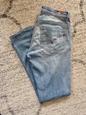 Dondup jeans george - Snygga ljusblå jeans med raka ben och klassiska femficksdetaljer. Jeansen har kontrastsömmar på bakfickorna och en diskret logga i rött vid linningen. Perfekta för en avslappnad och trendig look. OBS! Osäker på storlek då lappen blivit riven fråga om mått om du är intresserad!