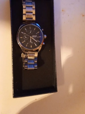 Klassisk silverfärgad klocka - Stilren klocka med silverfärgat metallarmband och svart urtavla. Urtavlan har flera små visare och tydliga markeringar. Klockan har en klassisk rund form och metallspänne. Perfekt accessoar för en clean look.