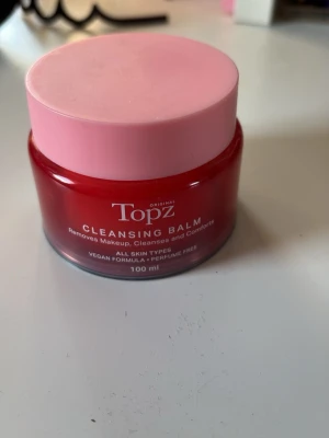 Topz Cleansing Balm 100 ml - Topz Cleansing Balm är en vegansk rengöringsbalm som tar bort smink och rengör huden. Kommer i en rund burk med röd kropp och rosa lock, innehåller 100 ml och passar alla hudtyper. Parfymfri formula . Endast testad.