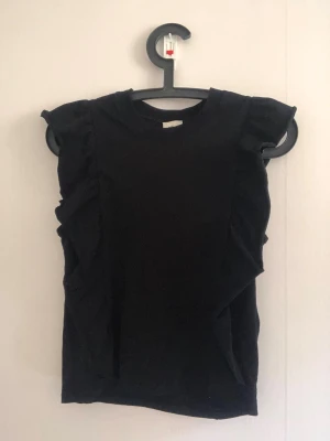 Svart ärmlös volang topp - Säljer en jätte söt scary topp med volanger lägst sidorna. Fick tyvärr inga bra bilder på tröjan, så skriv om du vill att jag ska skicka fler 💕