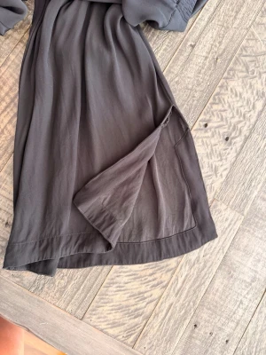 Mörkgrå omlottklänning Rodebjer - Snygga svarta vida byxor från Rodebjer i mjukt, lätt tyg. Splitt i benen. Avslappnad men stilren look. Perfekt för dig som gillar minimalistisk stil.