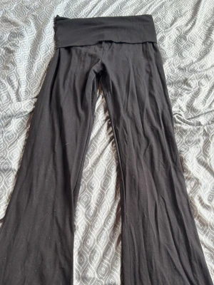 Svarta bootcut leggings - Säljer ett par svarta leggings med bootcut-ben och bred linning i midjan. De är gjorda i ett mjukt och stretchigt material som sitter skönt på kroppen. Perfekta för en avslappnad och trendig look.