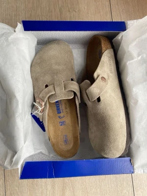Beige mockatofflor från Birkenstock - Säljer ett par snygga beige tofflor från Birkenstock. Sköna för utomhus aktiviteter eller vardaglig användning.