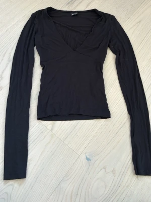 Svart långärmad v-ringad topp - En svart långärmad topp med v-ringning och figurnära passform. Tillverkad i mjukt bomullsmaterial, perfekt för att styla med jeans eller kjol. Enkel och stilren design utan mönster eller extra detaljer.