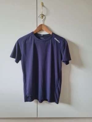 Mörkblå t-shirt från Craft strl 158/164 barn - Mörkblå t-shirt från Craft i storlek 158/164 barn. Klassisk rund halsringning och korta ärmar. Material 60% bomull, 40% polyester.