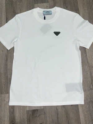 Prada  - Säljer en stilren vit Prada t shirt, helt ny och kommer med alla tillbehör som syns på bilden 