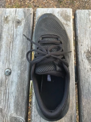 Svarta Under Armour sneakers - Säljer ett par svarta sneakers från Under Armour med mesh-ovandel och klassisk snörning. Skorna har en låg profil och diskret logga på sidan. Perfekta för dig som gillar sportig och stilren look.