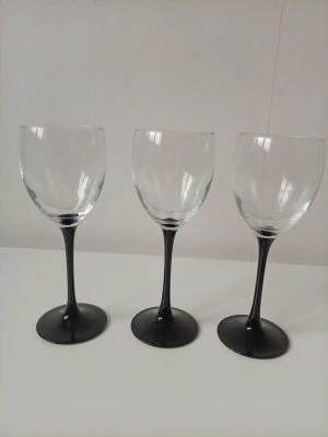 Tre vinglas med svart fot - Säljer tre stilrena vinglas med transparent kupa och svart fot. Glasen har en klassisk form med rundad kupa och smal stjälk. Perfekta till middagar eller som dekoration i vitrinskåpet ä nä tejp på den ena gå säkert få bort 