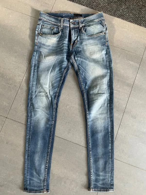 Tiger of Sweden - Säljer ett par blå jeans med tvättade detaljer. Jeansen har fem fickor, normal midja. Materialet är klassisk denim med stretch för extra komfort. Perfekta för en avslappnad och trendig look.