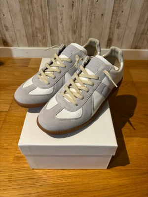 Maison Margiela - Maison Margiela i vitt och ljusgrått med beige snörning och gummisula. Skorna har en klassisk siluett med paneler i mocka och textil, perfekta för en clean och stilren look. Kvitto finns!