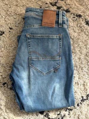 Blå slitna jeans från Jack & Jones - Snygga blå jeans från Jack & Jones med slitningar och hål på benen för en trendig look. Klassisk femficksmodell med normal passform och bälteshällor. Tillverkade i denim med ljus tvätt och detaljerade sömmar.