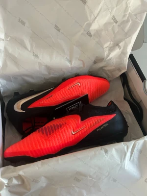 Nike Phantom röd/svarta fotbollsskor - Säljer ett par Nike Phantom fotbollsskor i en snygg röd och svart färgkombination. Ord pris 3099 kronor oh säljer för 2500 så priset är redan nedsatt med 600 kronor för skor i samma skick som en helt ny i butik, strorlek 39