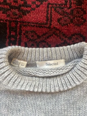 Ljusgrå stickad tröja Selected - Ljusgrå stickad tröja från Selected med rund halsringning och ribbade muddar vid ärmslut och nederkant. Enkel och stilren design som passar till det mesta. Perfekt för lager på lager och en klassiker i garderoben.