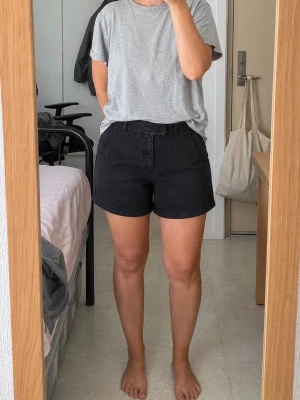 Svarta midwaist shorts i bomull - Säljer ett par svarta shorts i mjuk bomull med midwaist passform. Klassisk design med fickor på sidorna och enkel knappstängning framtill. Perfekta till sommaren och lätta att matcha med olika toppar.