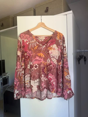 Odd Molly mönstrad blus i rosa/bruna toner - Säljer en vacker och bohemisk blus. Blusen har ett färgglatt mönster i rosa, brunt, orange och vitt. Långärmad modell med lös och ledig passform, perfekt till både vardag och fest! Materialet är lätt och luftigt, vilket gör den skön att bära. rån märket Odd Molly i storlek 3 som enligt deras storlekguide motsvarar en storlek L. Mycket fint skick, tråddragning finns. 