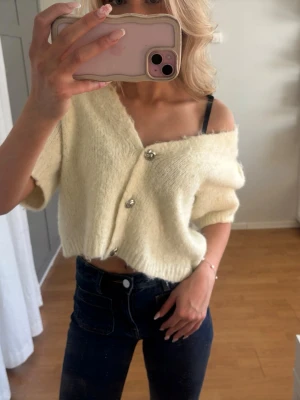 Ljusgul kortärmad stickad kofta - Söt och fluffig ljusgul stickad kofta med korta ärmar och v-ringning. Koftan har tre dekorativa knappar framtill och är croppad i modellen. Perfekt att styla till jeans eller kjol för en trendig look. Finns en sminkfläck på en axel, men det är inget man tänker på💗
