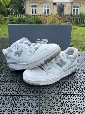 New Balance 550 vita sneakers - Snygga New Balance 550 sneakers i vitt med ljusgrå detaljer och klassisk N-logga på sidan. Skorna har en chunky sula och är tillverkade i läder och mesh för en fräsch och sportig look. Perfekta för dig som gillar stilrena och trendiga sneakers.