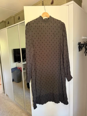 Svart långklänning med mönster - Säljer en svart/grå klänning med hög krage och långärmad design. Klänningen har ett diskret prickigt mönster och är tillverkad i ett tunt, transparent material. Perfekt för dig som gillar en elegant och stilren look. Från märket Odd Molly i storlek 3 som enligt deras storlekguide motsvarar en storlek L. Mycket fint skick, jag hittar inga synliga anmärkningar eller defekter. 