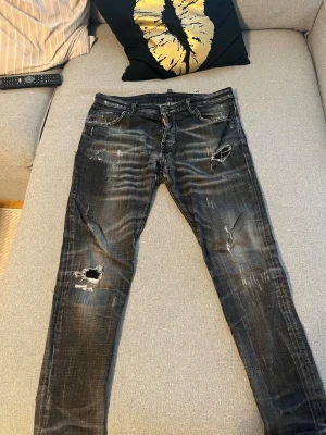 Svarta slitna jeans från Dsquared2 - Säljer ett par svarta jeans från Dsquared2 med slitningar och hål för en riktigt edgy look. Jeansen har slim fit, klassisk femficksmodell och coola detaljer som slitna partier och tvättade effekter. Perfekta för dig som gillar streetstyle och vill sticka ut.