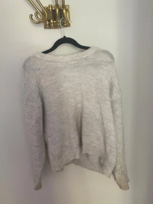Ljusgrå stickad tröja Gina Tricot - Mysig ljusgrå stickad tröja från Gina Tricot med avslappnad passform och rund halsringning. Tröjan har långa ärmar och ribbade muddar vid hals, ärmslut och nederkant. Perfekt för lager på lager under kyliga dagar. Passar storlek XS-S! 