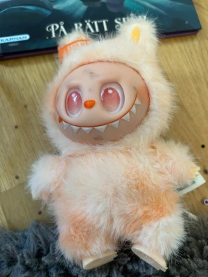 Söt fluffig monster-gosedjur - Unikt gosedjur med fluffig, ljusrosa päls och ett stort plastansikte med bredt leende och spetsiga tänder. Har stora rosa ögon, orange nos och små öron på huvudet. Perfekt för dig som gillar annorlunda och roliga mjukdjur.