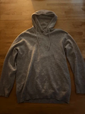 Stickad Hoodie - En stilren ljusgrå hoodie med huva och dragsnören. Tillverkad i mjukt stickat material som känns skönt mot huden. Hoodien har långa ärmar och ribbade muddar vid ärmslut och nederkant. Perfekt för en avslappnad look. Skriv vid funderingar 👍👍
