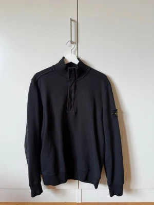 Svart halvzip sweatshirt Stone Island - Svart sweatshirt från Stone Island med halvzip och hög krage. Klassisk patch med logga på vänster ärm. Tröjan har ribbade muddar vid ärmslut och nederkant. Perfekt för en clean och stilren look.