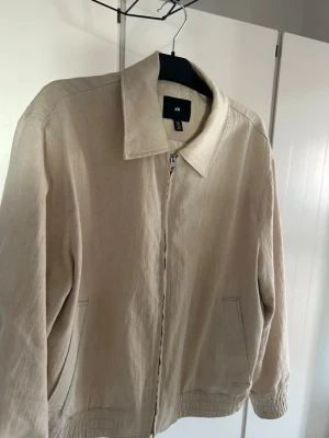 Beige overshirt jacka från H&M - Stilren beige overshirt jacka från H&M med dragkedja framtill och två sidofickor. Jackan har klassisk krage och är tillverkad i ett lätt material som passar perfekt för vår och sommar. Enkel och clean design som funkar till det mesta.