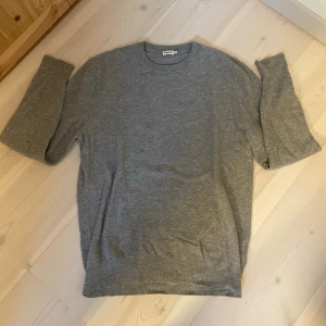 Stickad Tröja | FILIPPA K. - En enkel och stilren grå stickad tröja med rund halsringning och långa ärmar från Filippa K’s herravdelning. Perfekt att matcha med jeans för en clean look. Tröjan har en mjuk känsla och klassisk passform.