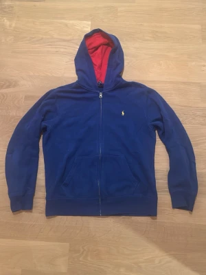 En blå Ralph lauren tröja i  - En blå ralph lauren tröja i storlek 14-16. Den är i bra skick men det finns en liten fläck på vänster sida av dragkedjan som syns på nära håll