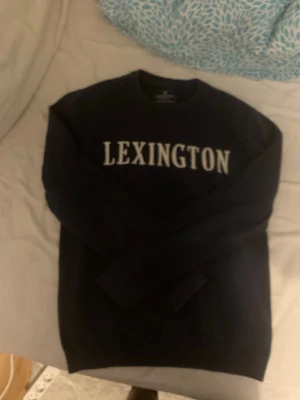 Svart Lexington tröja med tryck - Snygg svart tröja från Lexington med vit text över bröstet. Klassisk rund halsringning och långa ärmar. Perfekt för dig som gillar enkel och stilren design med tydlig logga framtill. Är Storlek M men mer som en S 