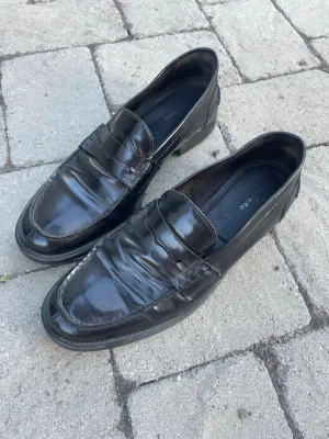 Svarta loafers i skinn från rizzo - Klassiska svarta loafers från rizzo i blankt skinn. Snygg penny loafer-design med rundad tå och diskret söm längs kanten. Perfekta för dig som gillar stilrena och tidlösa skor med en clean look.