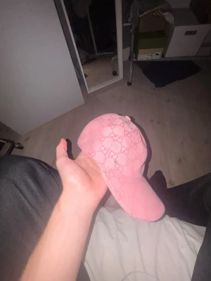 Gucci keps - Säljer en rosa keps från Gucci med det klassiska GG-mönstret över hela kepsen. Kepsen har böjd skärm och justerbart spänne bak. Materialet är canvas med insida i ljus textil. Perfekt för dig som vill sticka ut med en lyxig accessoar.