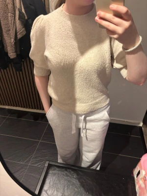 Beige puffärm stickad tröja - Säljer en beige stickad tröja med puffärmar och ribbade muddar vid ärmslut och hals. Tröjan har en mjuk struktur och kortare ärmar som slutar strax ovanför armbågen. Perfekt för dig som gillar en enkel men trendig look.