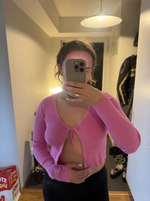 Rosa ribbad croppad kofta - Trendig rosa ribbad kofta med croppad passform och knytning framtill. Djup v-ringning och långa ärmar ger en snygg och avslappnad look. Perfekt att styla över ett linne eller topp för en cool vibe.