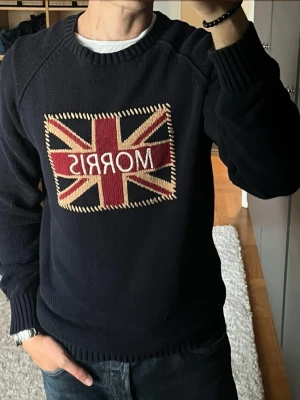 Morris tjocktröja med flagga i marinblå - stl L - Morris tjocktröja i marinblå, storlek L. 100% bomull, raglanärmar med ribbad hals, muddar och nederkant, broderad Union Jack på bröstet.  Använd men i mycket fint skick, inga hål eller fläckar. Personen på bilden är 189cm, väger 78kg.  Rök- och djurfritt hem. Skriv gärna om du vill ha fler bilder eller undrar något!