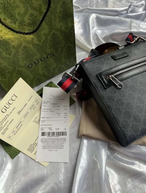 Gucci axelväska med monogram och ränder - Snygg axelväska från Gucci i svart och grått med klassiskt GG-monogram och en framficka med dragkedja. Axelremmen är justerbar och har röd-blåa ränder för en sportig touch. Väskan är tillverkad i slitstarkt material och har detaljer i svart läder.