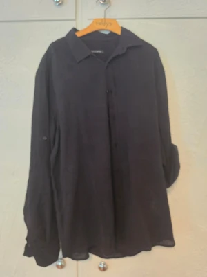 Svart oversized skjorta med knappar - Svart oversized skjorta med långa ärmar och knappar framtill. Skjortan har en klassisk krage och är tillverkad i ett lätt tyg, perfekt för en avslappnad stil. Ärmarna kan rullas upp och fästas med knapp.