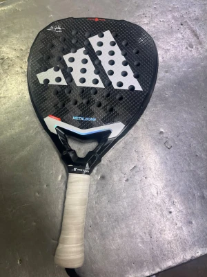 Adidas Metalbone padelracket - Säljer ett Adidas Metalbone padelracket med svart och vit design samt stora vita loggor. Racket har rund form, många hål och grepp med vitt lindat handtag. Perfekt för dig som vill ta ditt padelspel till nästa nivå.
