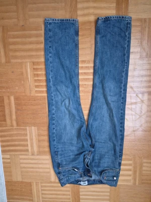 Blå raka jeans med hög midja - Säljer ett par klassiska blå jeans med raka ben och hög midja. Jeansen har dragkedjegylf, fem fickor och kontrastsömmar. Perfekta till vardags och passar till det mesta. Storlek 157, midjemått 30.