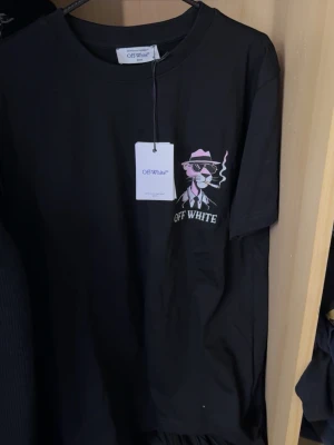 Svart Off White t-shirt med tryck - Svart t-shirt från Off White med en stor tryckt design av Pink Panther i kostym och hatt, rökandes en cigarr. T-shirten har rund hals och korta ärmar. Snygg och cool streetstyle med vit text och detaljer i rosa och svart. Storlek S men passar Storlek M 