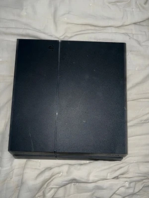 Playstation 4 svart spelkonsol - Säljer en svart Playstation 4 spelkonsol med stilren, kantig. Perfekt för gaming och underhållning hemma. Skulle säga att den fortfarande är i rätt så bra skick och fungerar. Inga kontroller följer med men kablar ingår. 3 spel följer med. Vid snabb affär kan priset diskuteras 