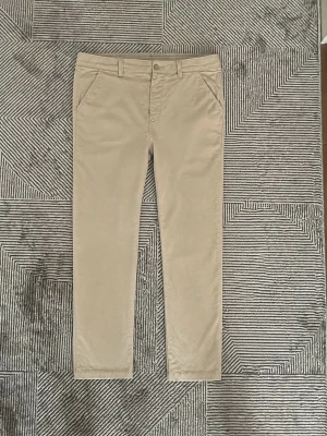 Beige chinos med rak passform - Snygga beige chinos med rak passform och klassiska sidofickor. Byxorna har bälteshällor och stängs med knapp och dragkedja. Tillverkade i ett mjukt och bekvämt bomullsmaterial som passar perfekt till en avslappnad stil.