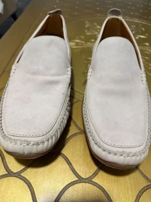 Of white loafers i mocka från Timberland - Snygga of white loafers i mocka från Timberland med klassisk slip-on design och dekorativa sömmar runt tån. Skorna har en låg profil och diskret Timberland-logga på hälen. Insidan är fodrad i ljust läder för extra komfort. Använts några enstaka gånger. 