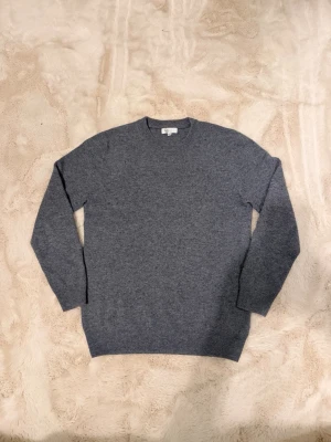 Grå stickad merinoull sweater - En stilren grå stickad tröja med rund halsringning och långa ärmar. Tröjan har en klassisk passform och är tillverkad i mjuk merinoull som känns skön mot huden. Perfekt att matcha med jeans för en enkel och snygg look.