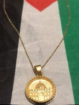 Guldfärgat halsband med kupolberlock - Snyggt halsband i guldfärg med en rund berlock som har ett ingraverat motiv av en kupolbyggnad. Kedjan är tunn och elegant, och berlocken har en tvinnad kant som ger extra detalj. Perfekt accessoar för att lyfta din stil.