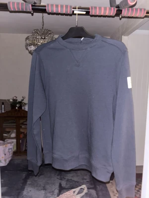 Mörkblå sweatshirt från sailracing - En enkel och stilren mörkblå sweatshirt med rund hals och lång ärm. Tröjan har en ljus patch på ena ärmen och ribbade muddar vid ärmslut och nederkant. Perfekt för en avslappnad look. 