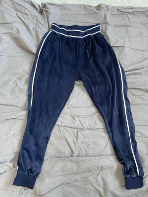 La Vichy dress - Mörkblå mjukisbyxor i velour med vita ränder längs sidorna och bred resår i midjan. Byxorna har muddar vid bensluten och en sportig look. Perfekta för en avslappnad stil.